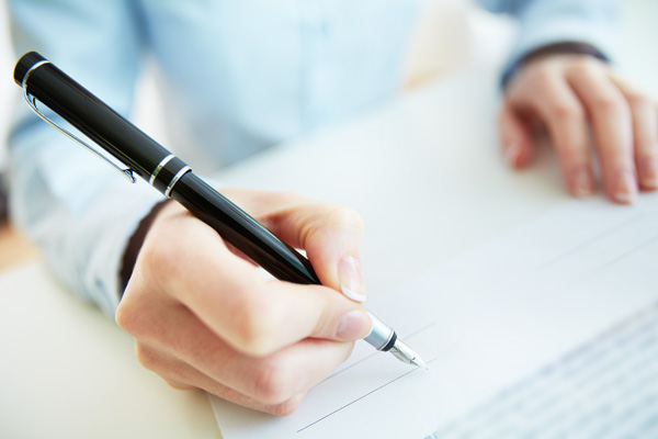A man's signing paper with a pen in his hand.