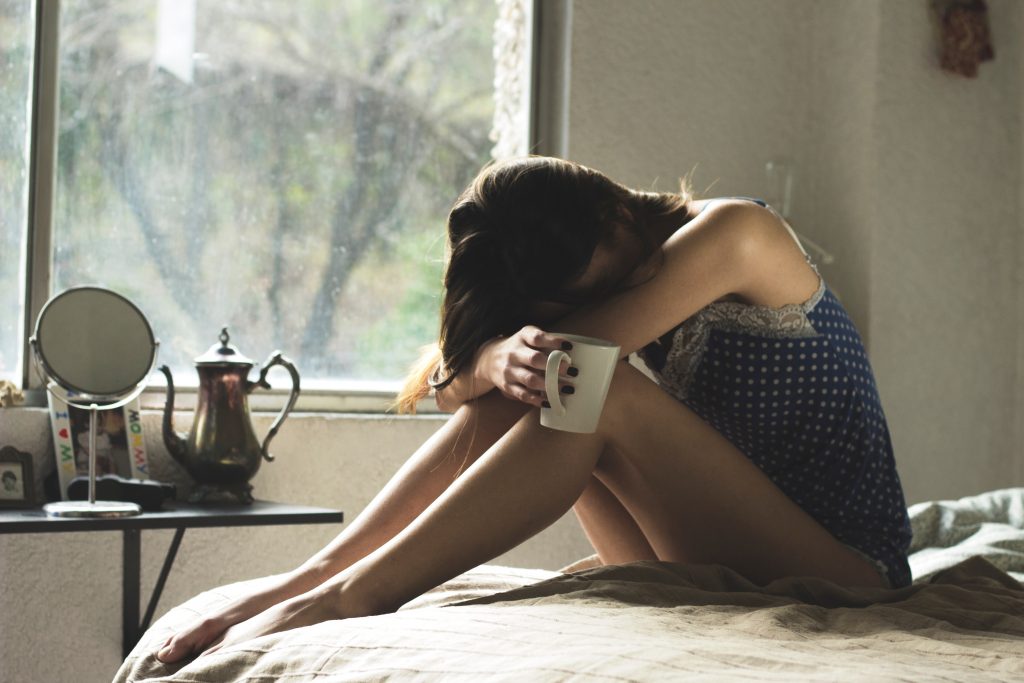 woman on bed with head in arms on knees due to nausea