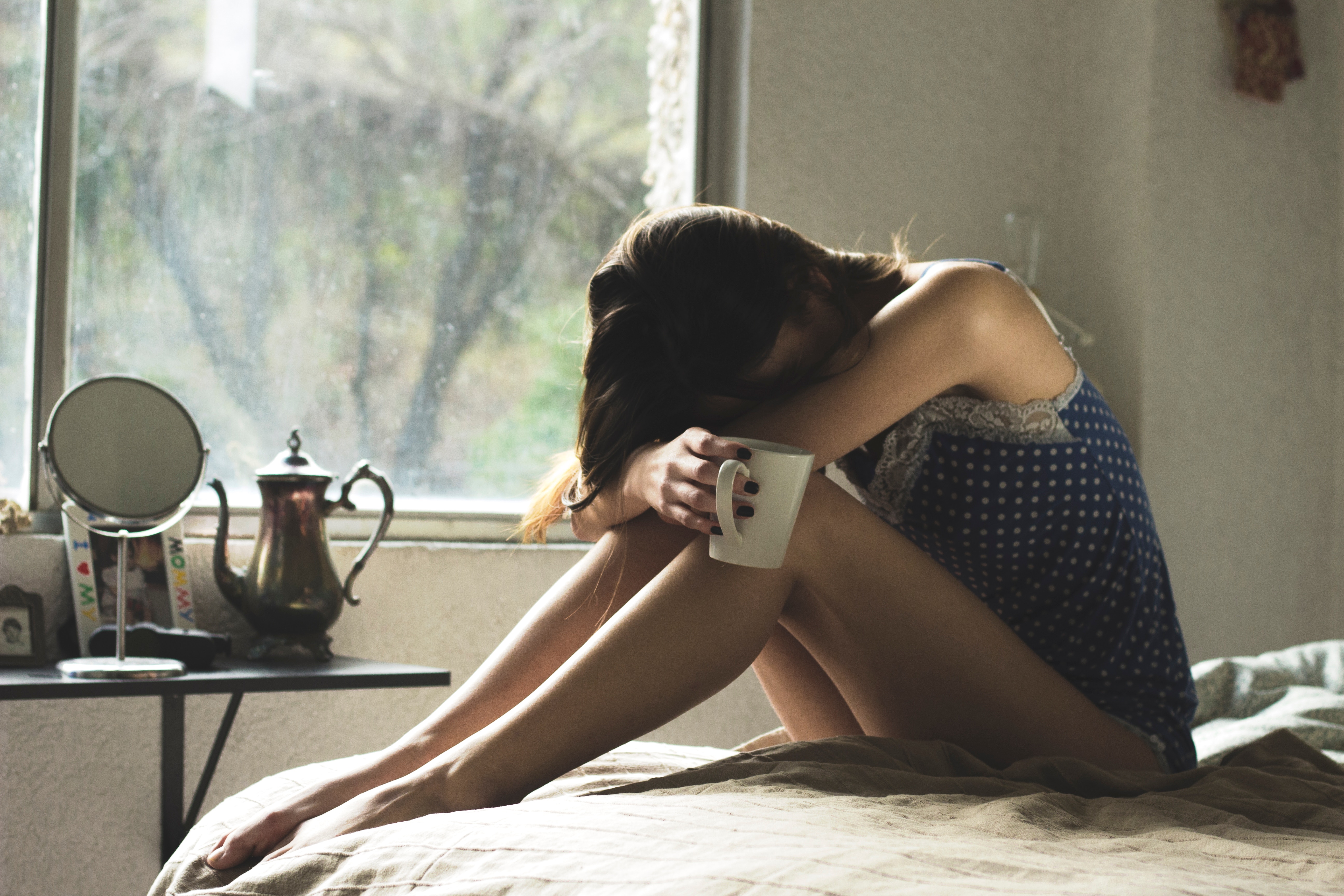 woman on bed with head in arms on knees due to nausea